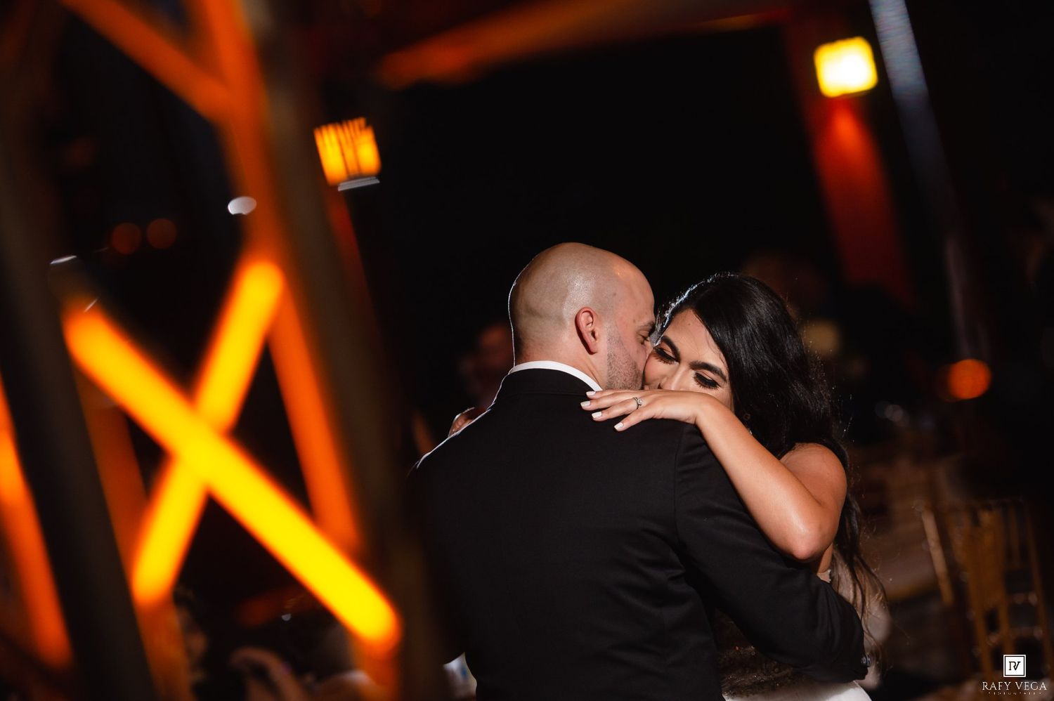 Couple sharing an intimate first dance embrace at a romantic wedding reception with warm amber lighting.