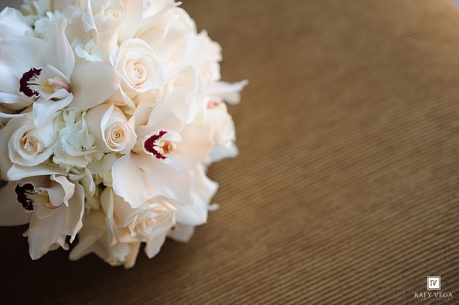 Elegant bridal bouquet of white roses, orchids, and hydrangeas arranged on a golden textured surface.