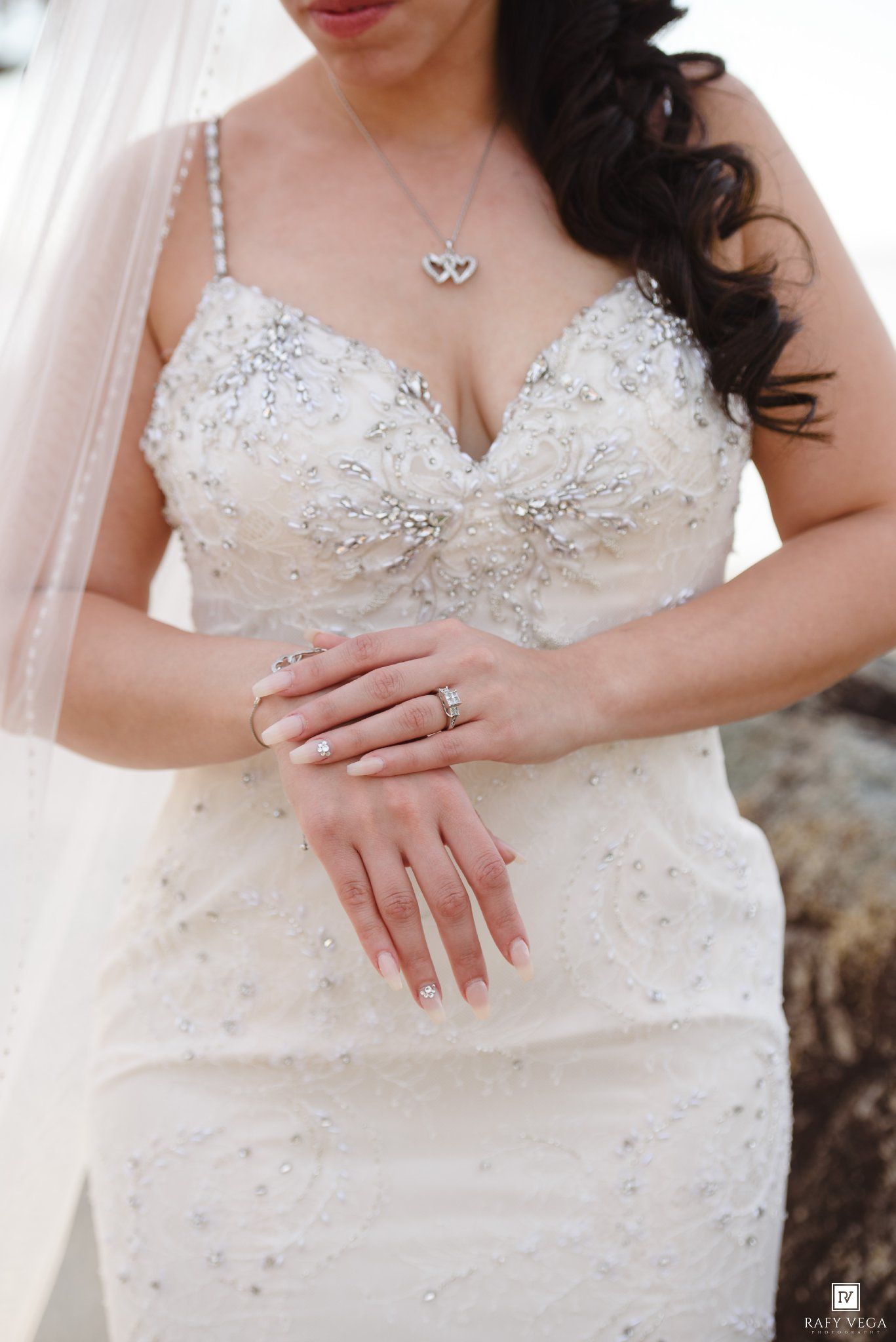 Close-up of bride in beaded lace wedding gown showing diamond ring, bracelet and heart necklace.