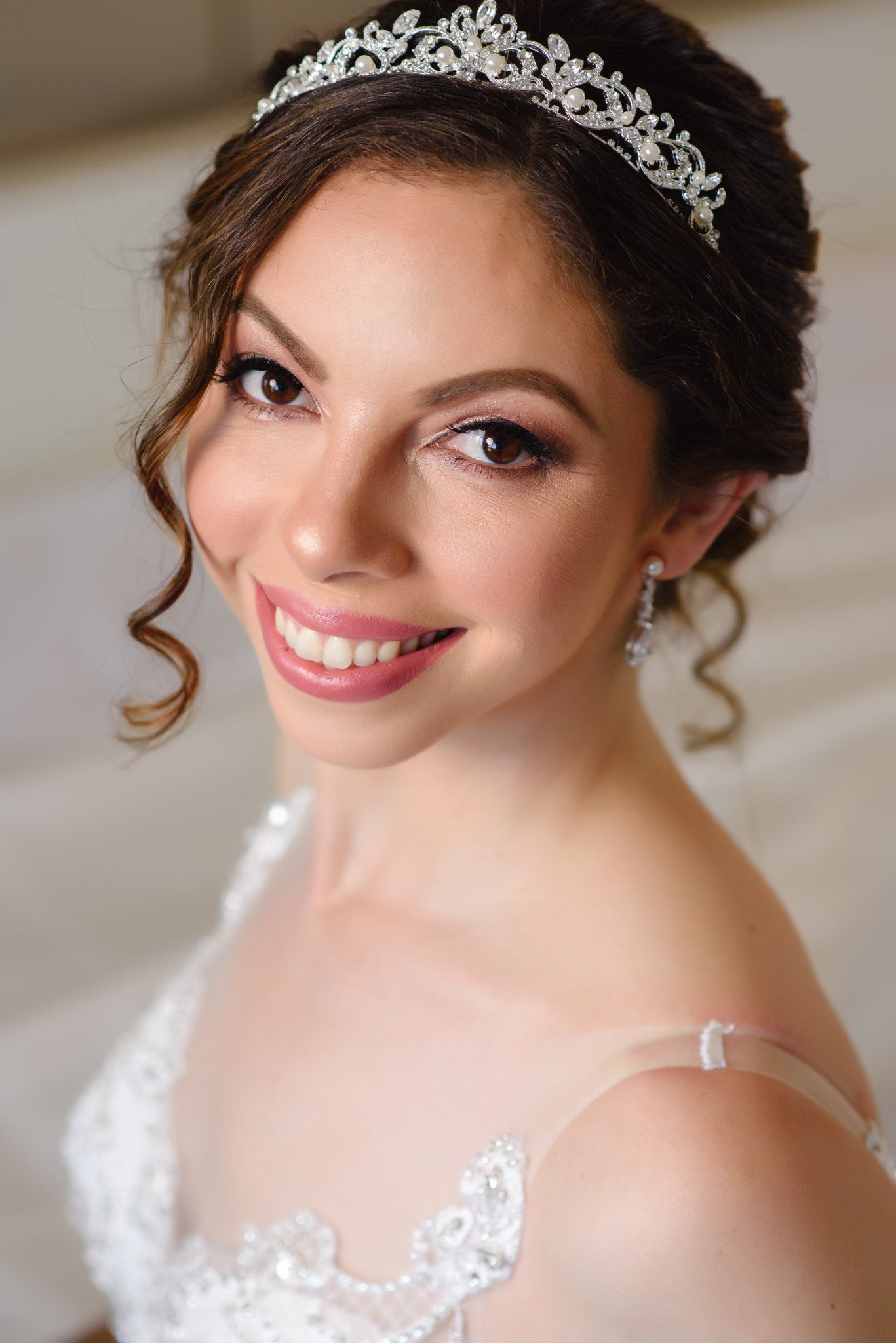Smiling bride wearing a silver tiara, pearl earrings, and white lace wedding dress with elegant updo hairstyle.