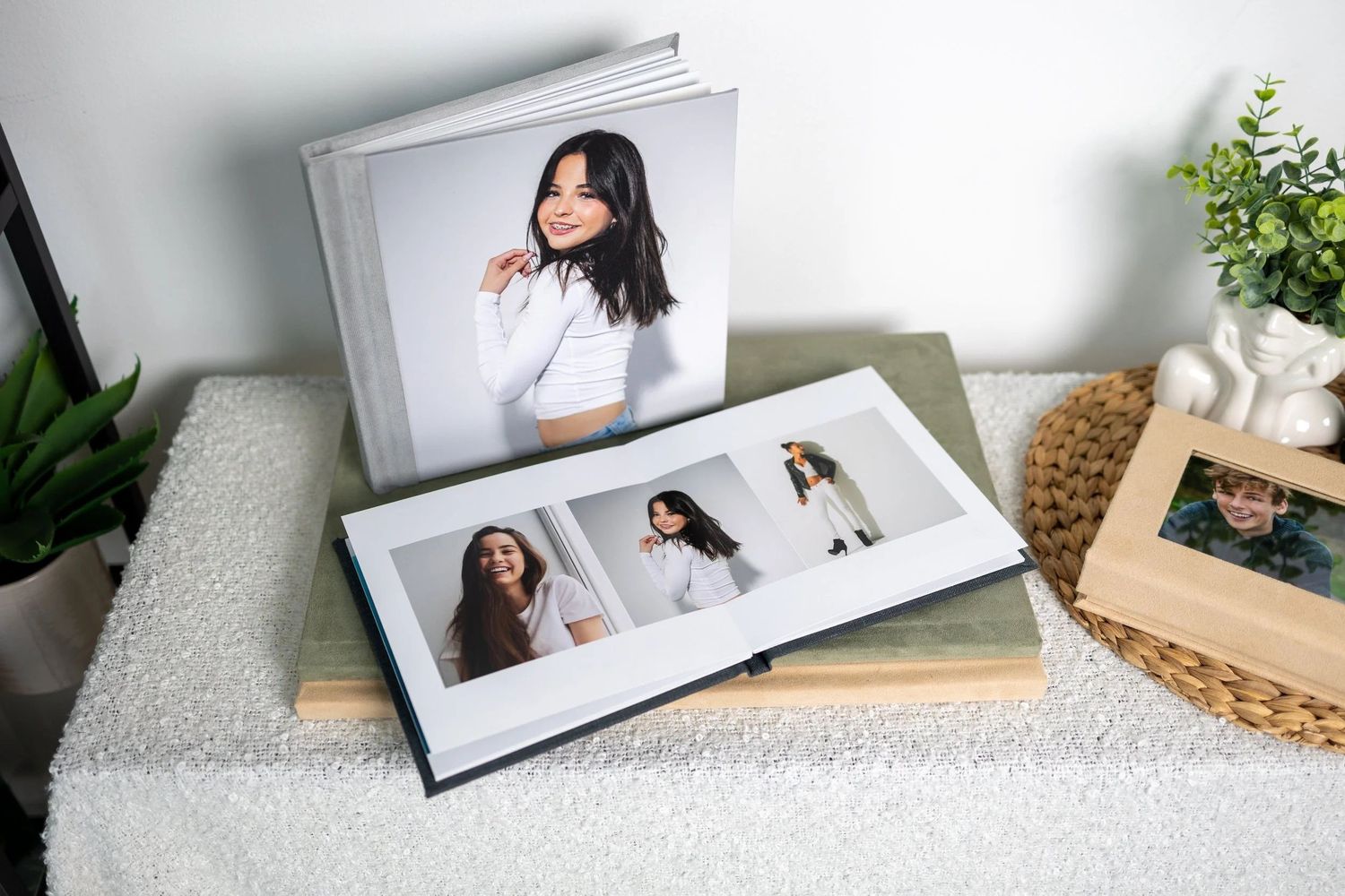 Two open photo books displaying professional portraits of women, arranged on a textured surface beside a green plant.