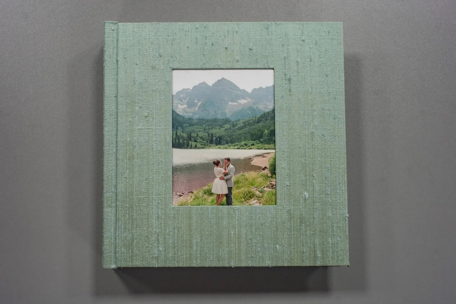 Green linen hardcover photo album with a couple embracing near a mountain lake on the cover.
