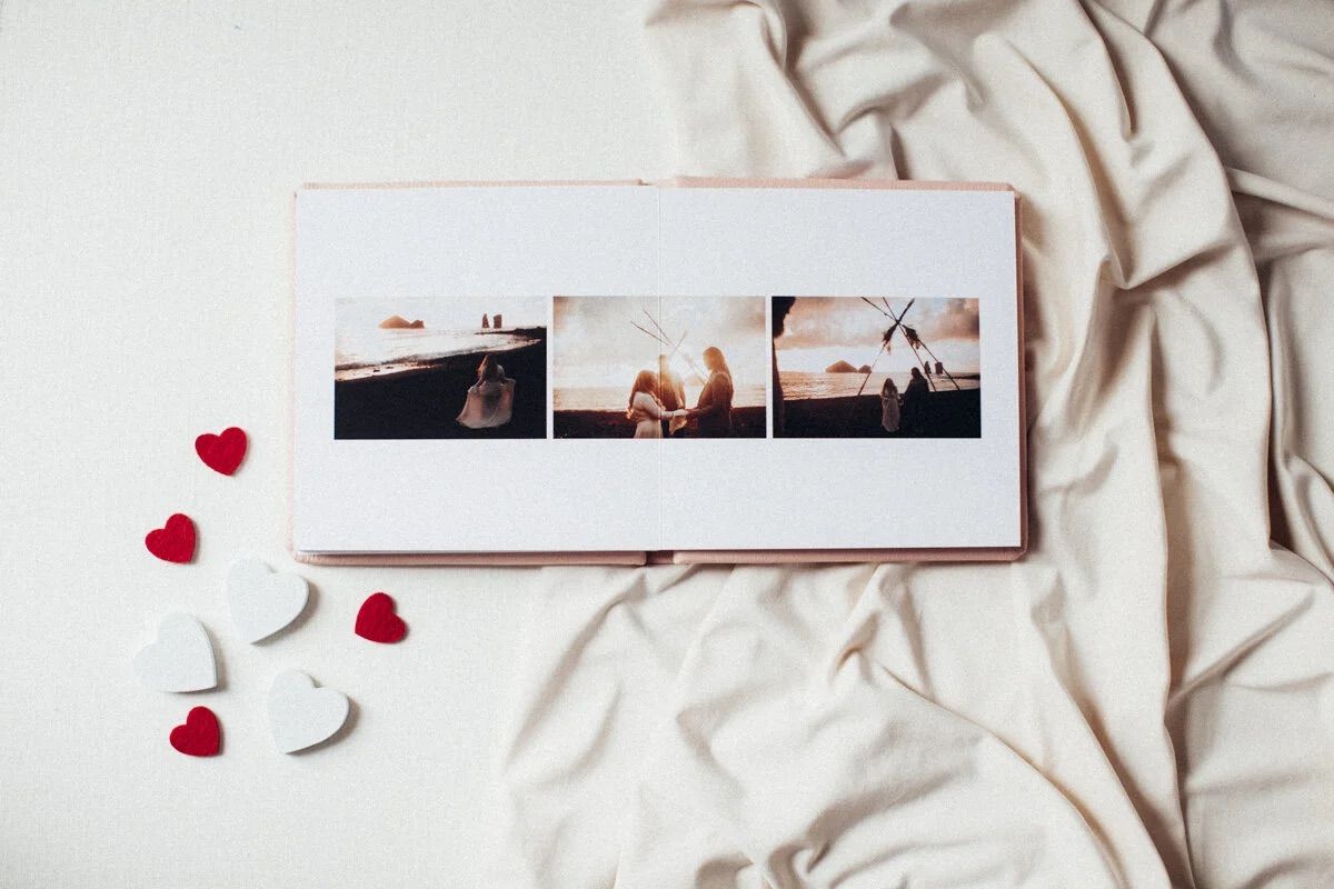 A romantic photo album with three wedding pictures lies on cream fabric, surrounded by red and white heart decorations.