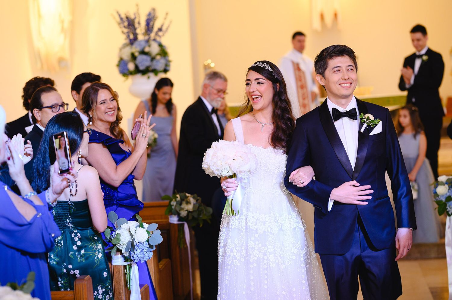 Newlywed couple walks down church aisle smiling as guests celebrate their wedding ceremony.