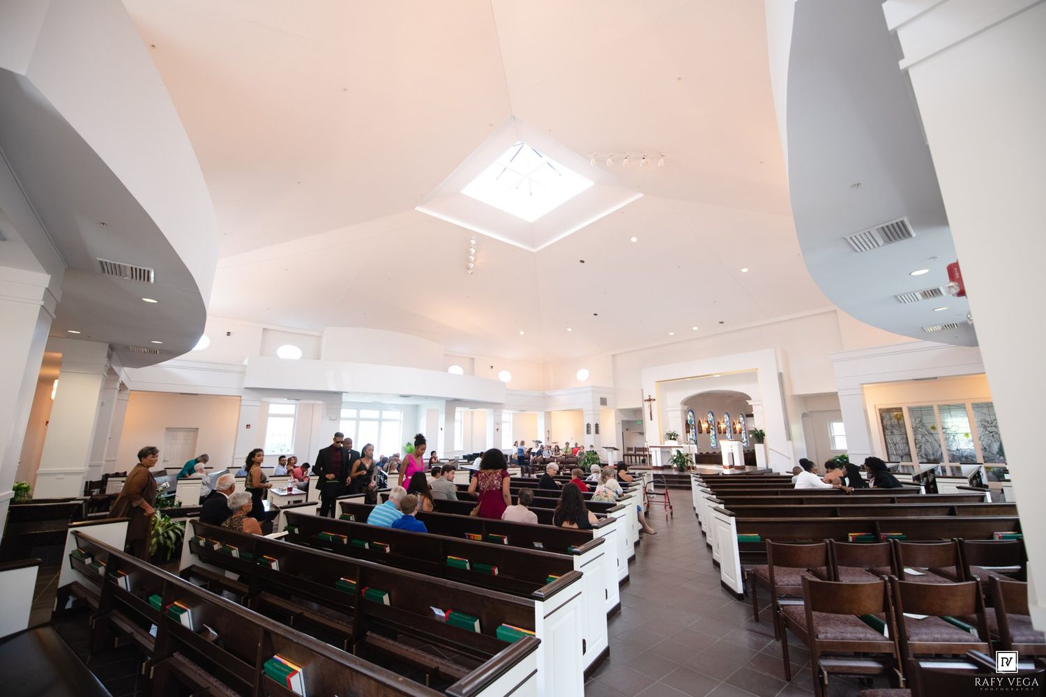 Bright church interior with white vaulted ceilings, wooden pews, and congregation gathered for a service.