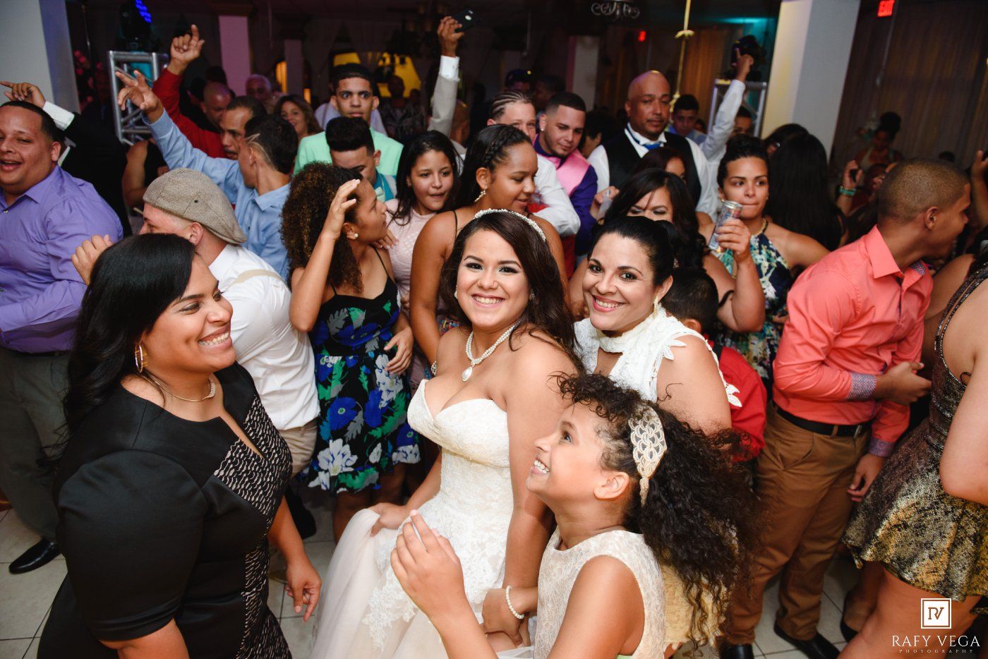 Bride smiling with guests on wedding reception dance floor, surrounded by family and friends celebrating.