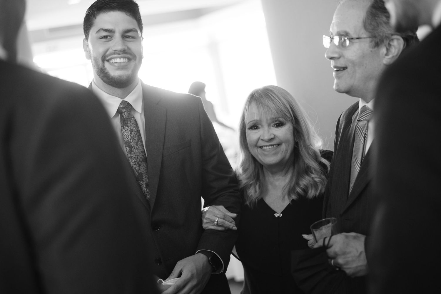 Black and white photo of three smiling people at a formal event, two men and a woman posing together.
