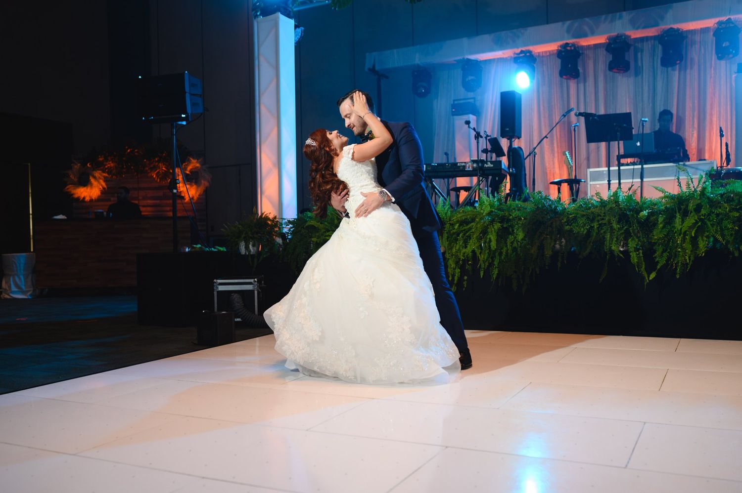 Bride and groom share romantic first dance, groom lifting bride in white ballgown at elegant wedding reception.