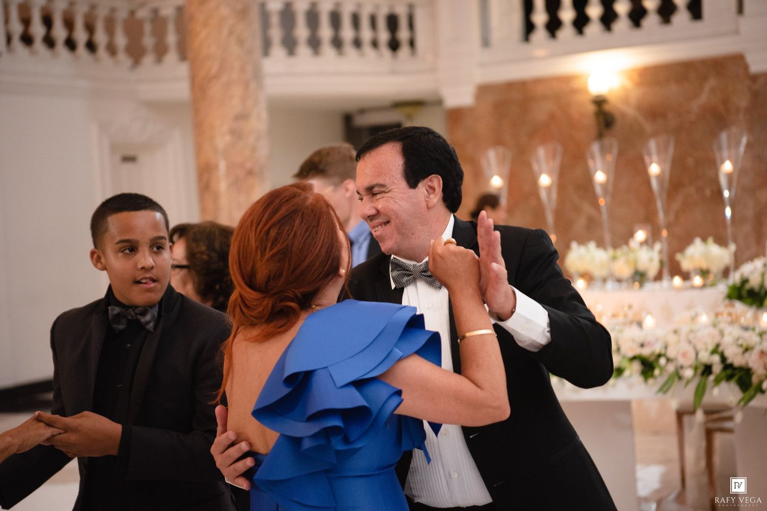 Couple dancing elegantly at a wedding reception in a grand ballroom with floral decorations.