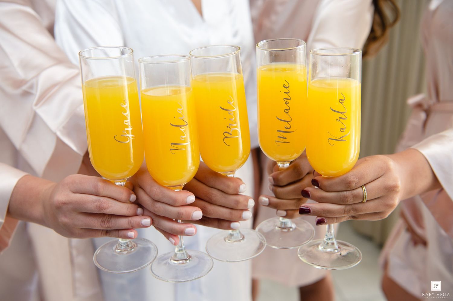 Bridesmaids in blush robes toasting with personalized champagne flutes filled with mimosas.