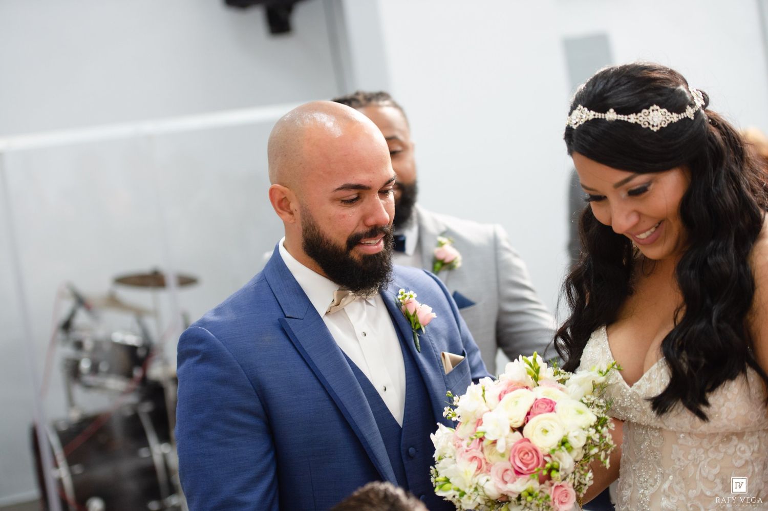 Bride and groom share a tender moment at altar, bride holding pink and white bouquet in lace gown.