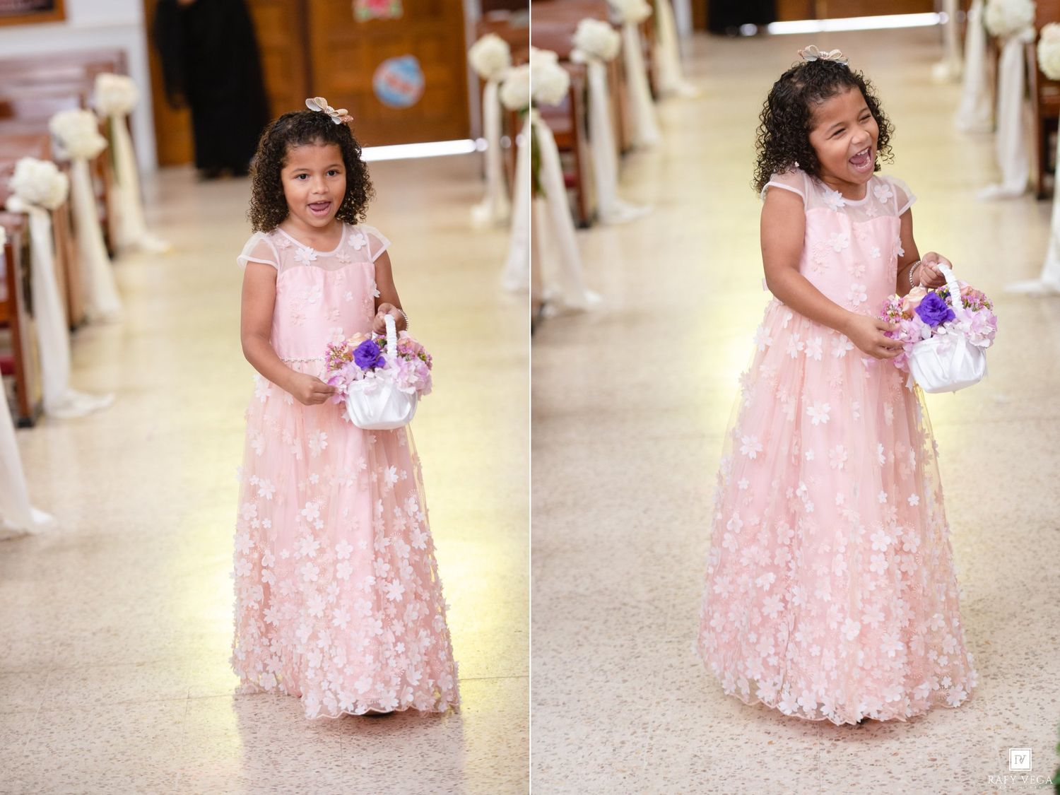 Young flower girl in pink lace gown holds floral basket while walking down church aisle at wedding ceremony.