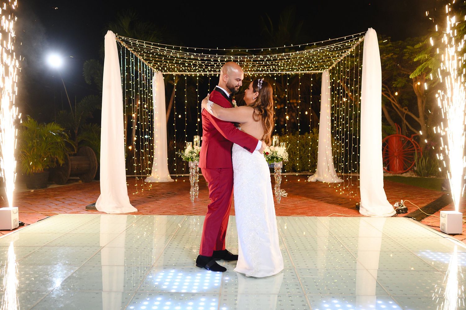 Bride and groom sharing first dance on illuminated floor with sparkling light curtain backdrop.