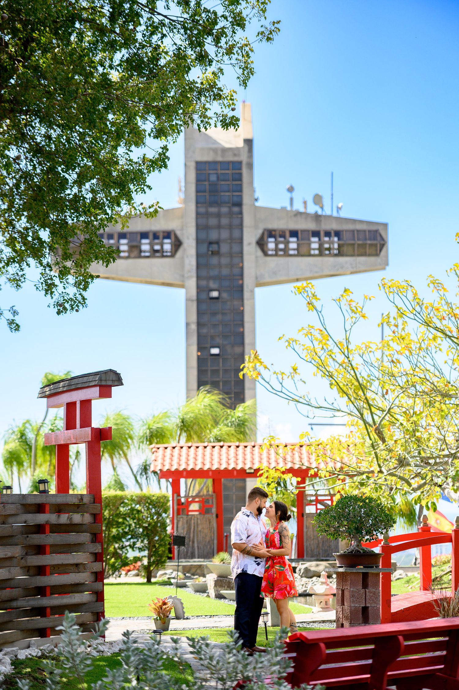 Couple sharing a romantic moment in a Japanese garden with a large cross monument in the background.