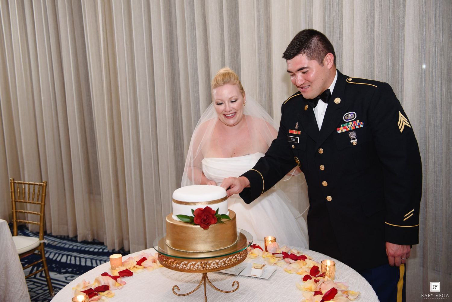Military groom in dress uniform and bride in white gown cutting wedding cake at elegant reception.