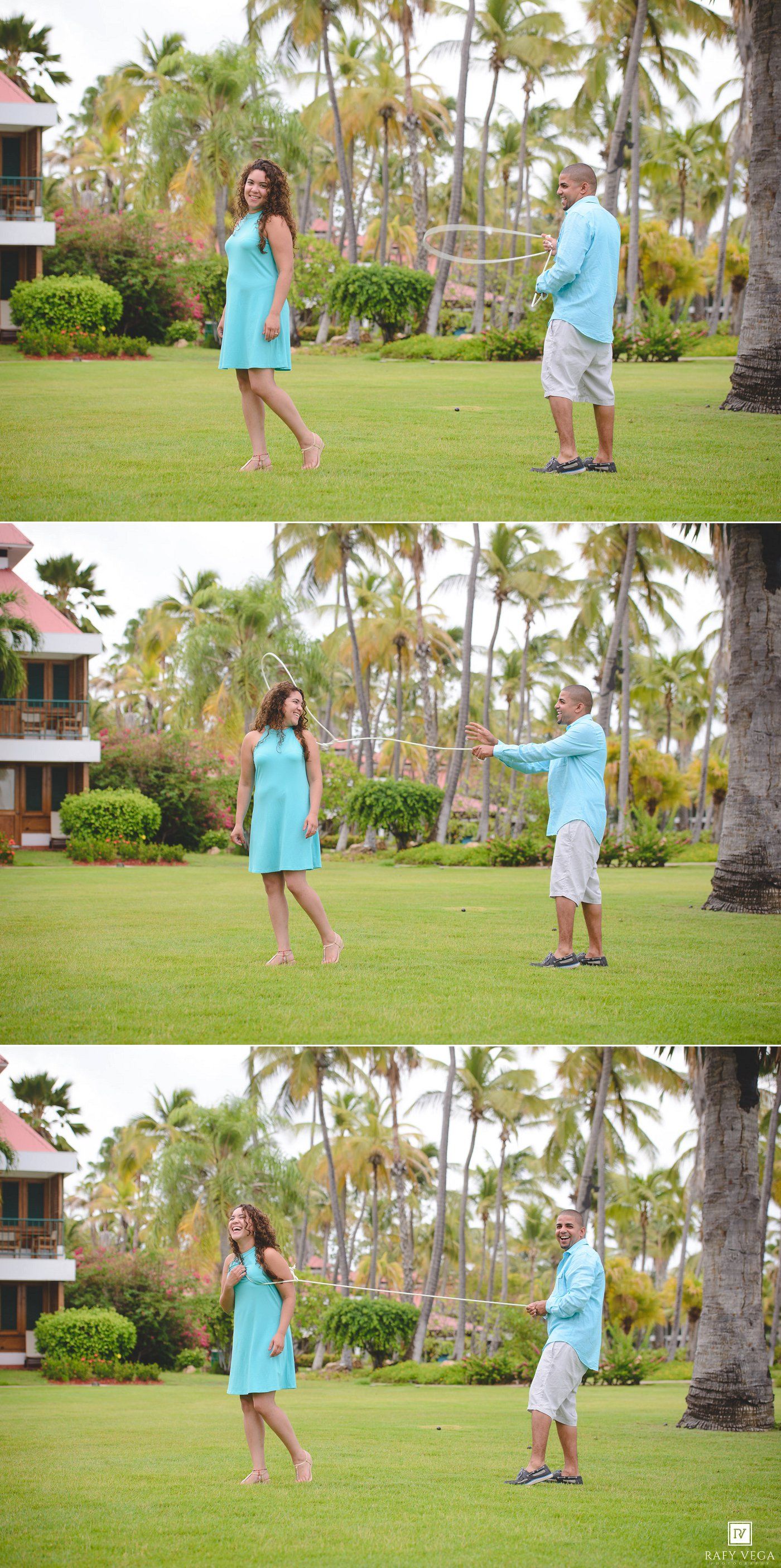 A couple plays with a hula hoop on a lush tropical resort lawn surrounded by palm trees.