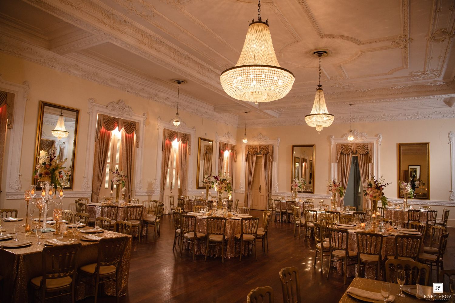Elegant wedding reception hall with crystal chandeliers, gold chiavari chairs, and romantic candlelit round tables.