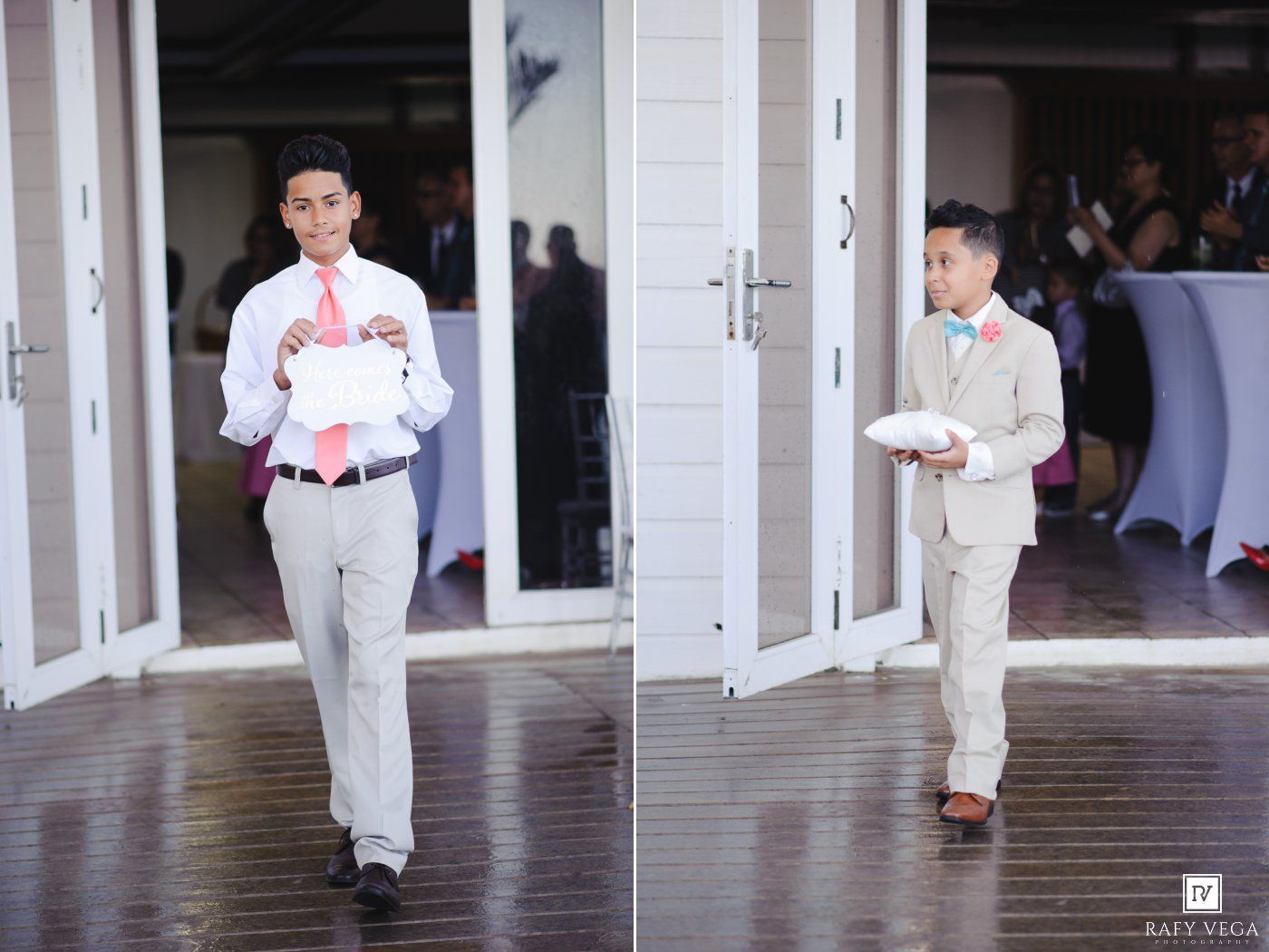 Young ring bearer in gray suit and coral tie walks down aisle at elegant wedding venue carrying ring pillow.