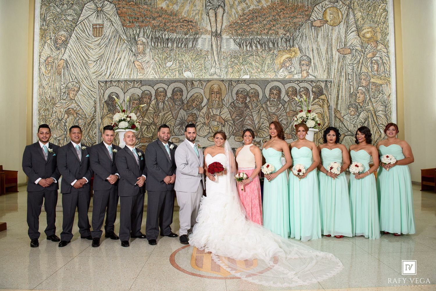 Wedding party poses in church with mosaic backdrop, groomsmen in gray suits and bridesmaids in mint green gowns.