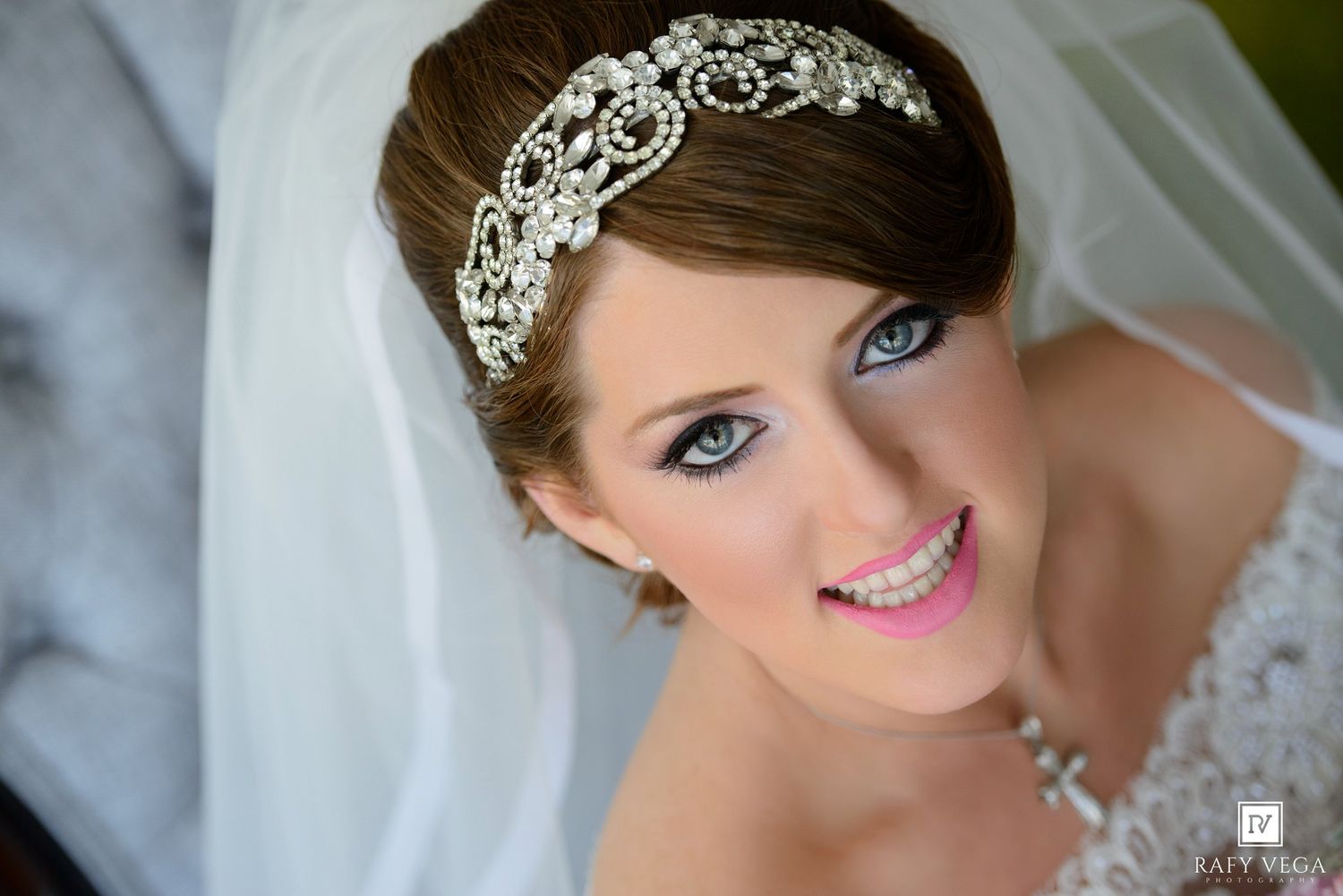 Bride wearing crystal rhinestone headband with veil, blue eyes, pink lips, elegant wedding makeup and updo hairstyle.
