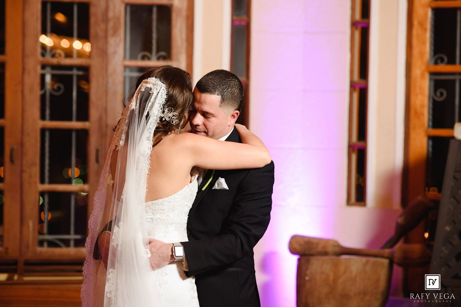 Bride and groom share an emotional first dance embrace, bride in white gown with veil, groom in black tuxedo.