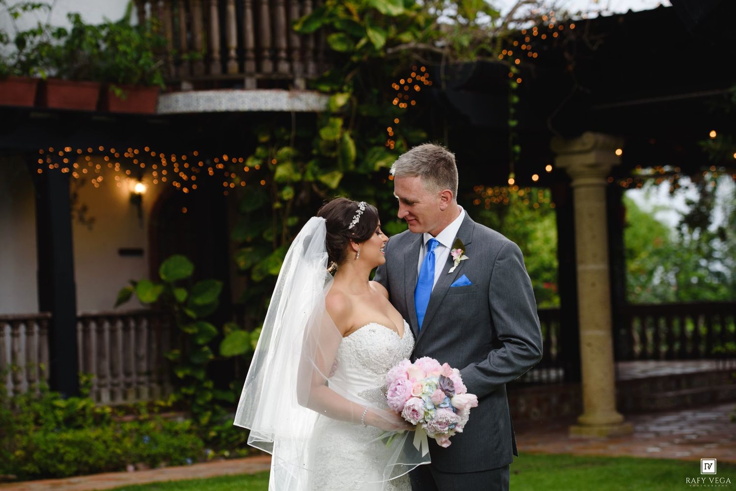 Bride and groom share a romantic moment in a lush garden venue adorned with string lights during their outdoor wedding.