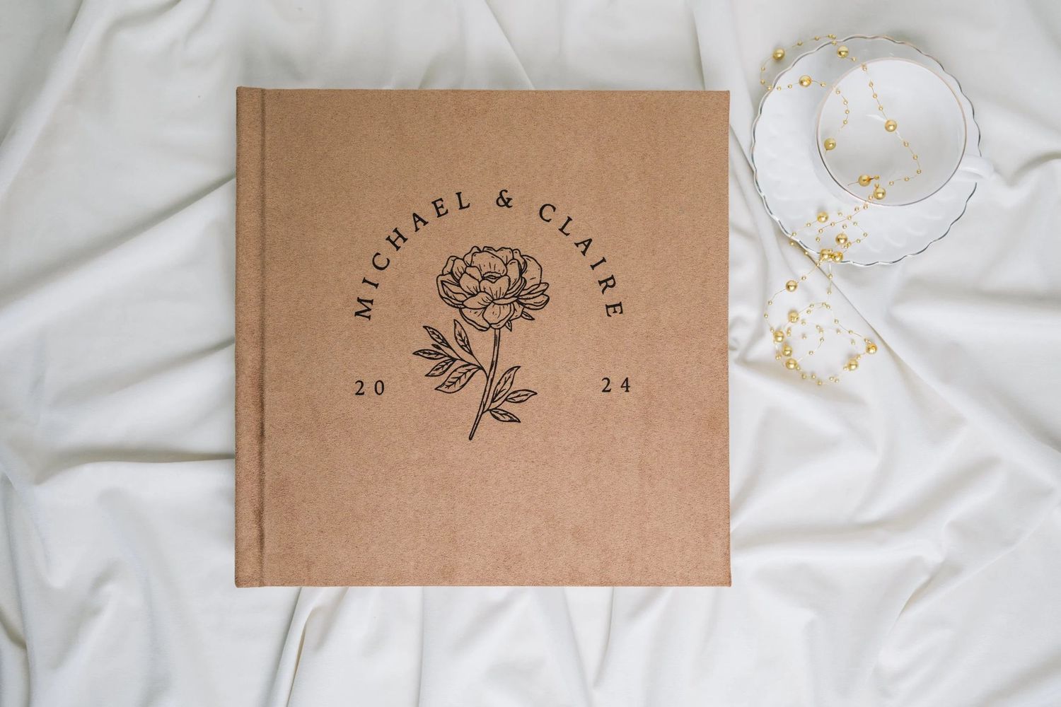 Kraft brown wedding guest book embossed with Michael & Claire 2024 and a peony flower illustration.