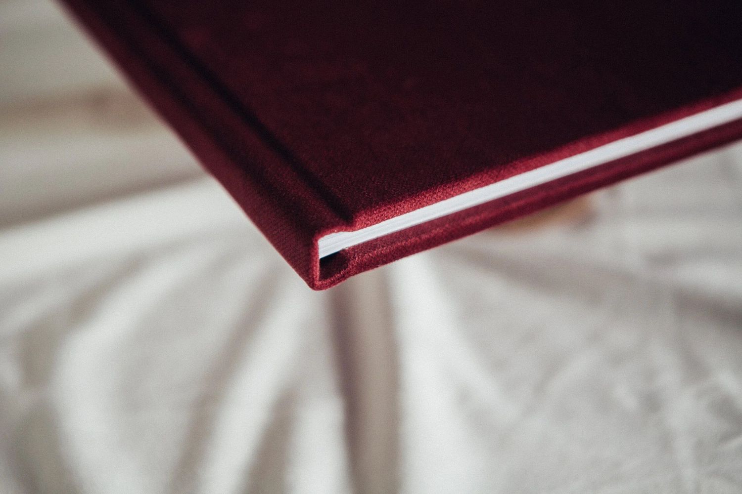 Close-up of a burgundy hardcover book with white spine resting on a white fabric surface.