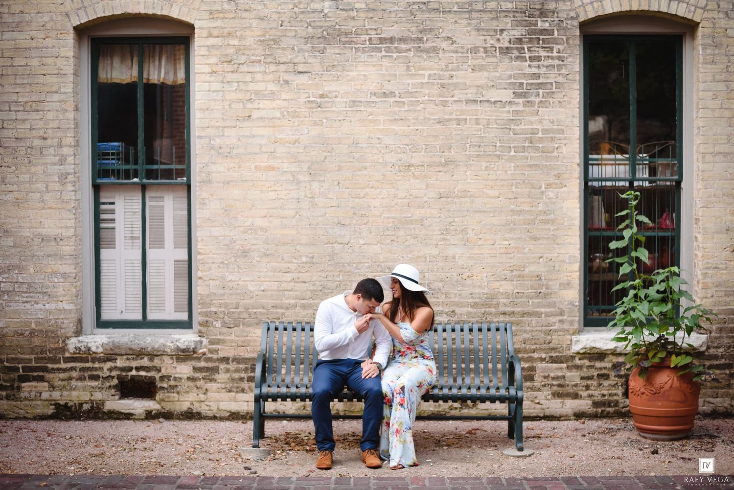 Couple sitting close together on a bench against a brick wall, sharing an intimate moment outdoors.