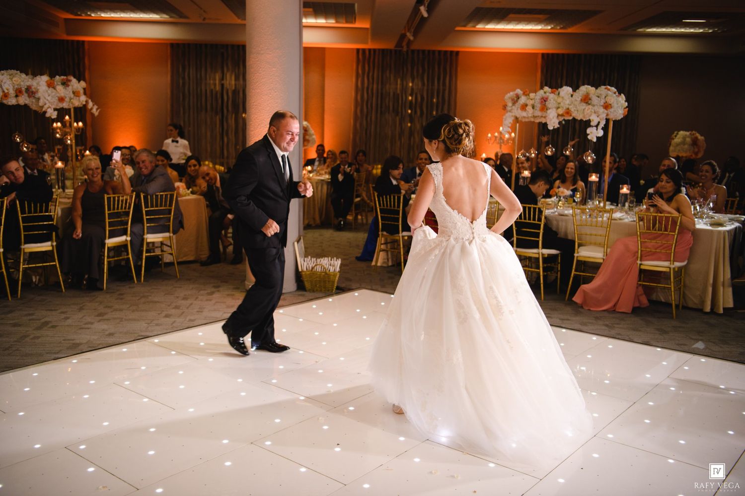 Bride and groom share their first dance on a white LED dance floor at an elegant wedding reception.