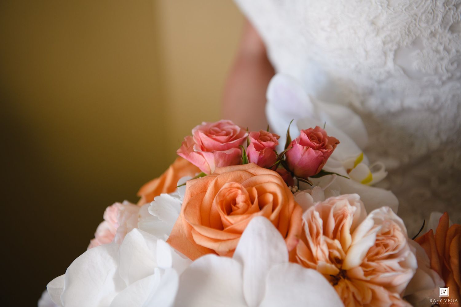 Close-up of a bridal bouquet featuring peach and pink roses with white petals, held by a bride in a lace wedding dress.