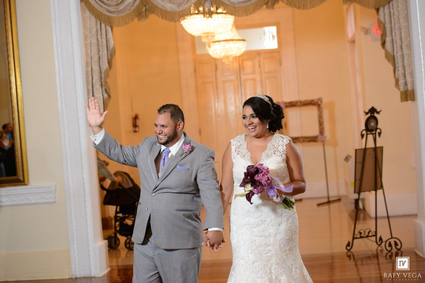 Newlywed couple holding hands and waving as they enter their elegant wedding reception venue.