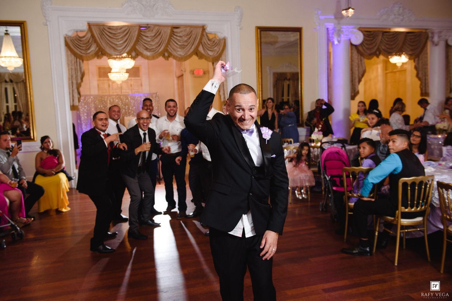 Man in tuxedo celebrates on dance floor at elegant wedding reception venue.