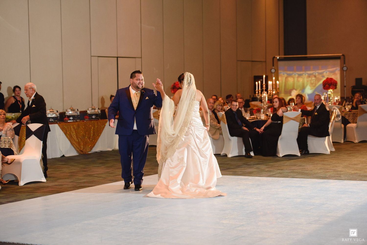 Bride and groom share their first dance on a white dance floor at a elegant wedding reception.