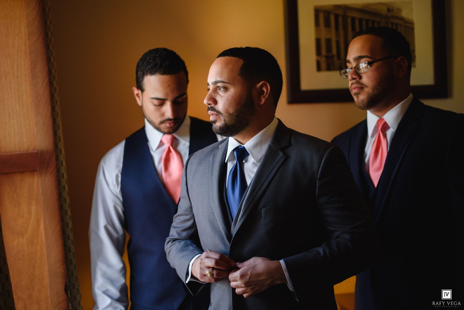 Three groomsmen in suits adjusting their attire before a wedding ceremony.