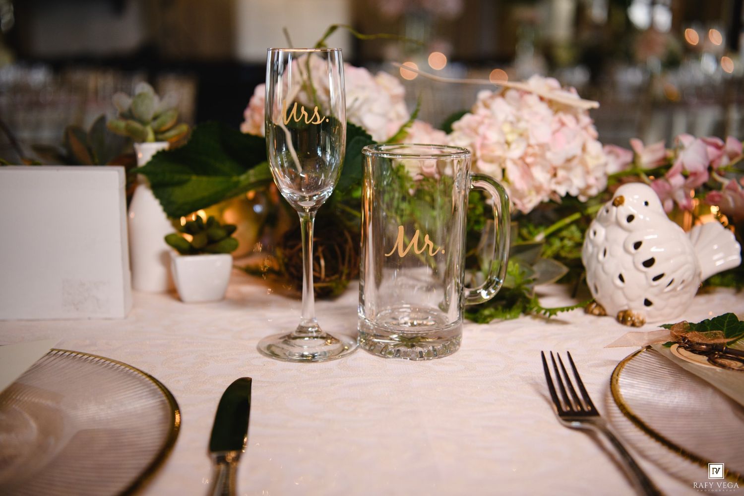Elegant wedding table setting with Mr. and Mrs. glassware, pink hydrangeas, and gold accents on a white linen tablecloth.
