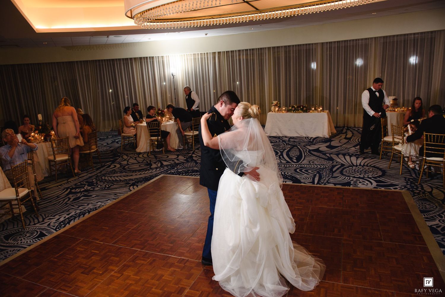 Bride and groom share their first dance on a wooden dance floor at an elegant wedding reception venue.