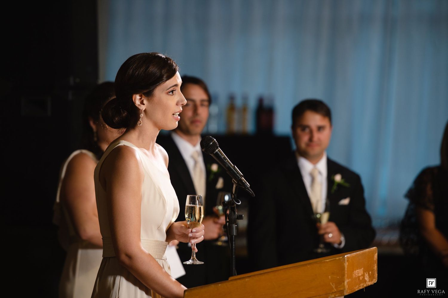 Woman in white dress giving a toast with champagne glass at a formal wedding reception event.