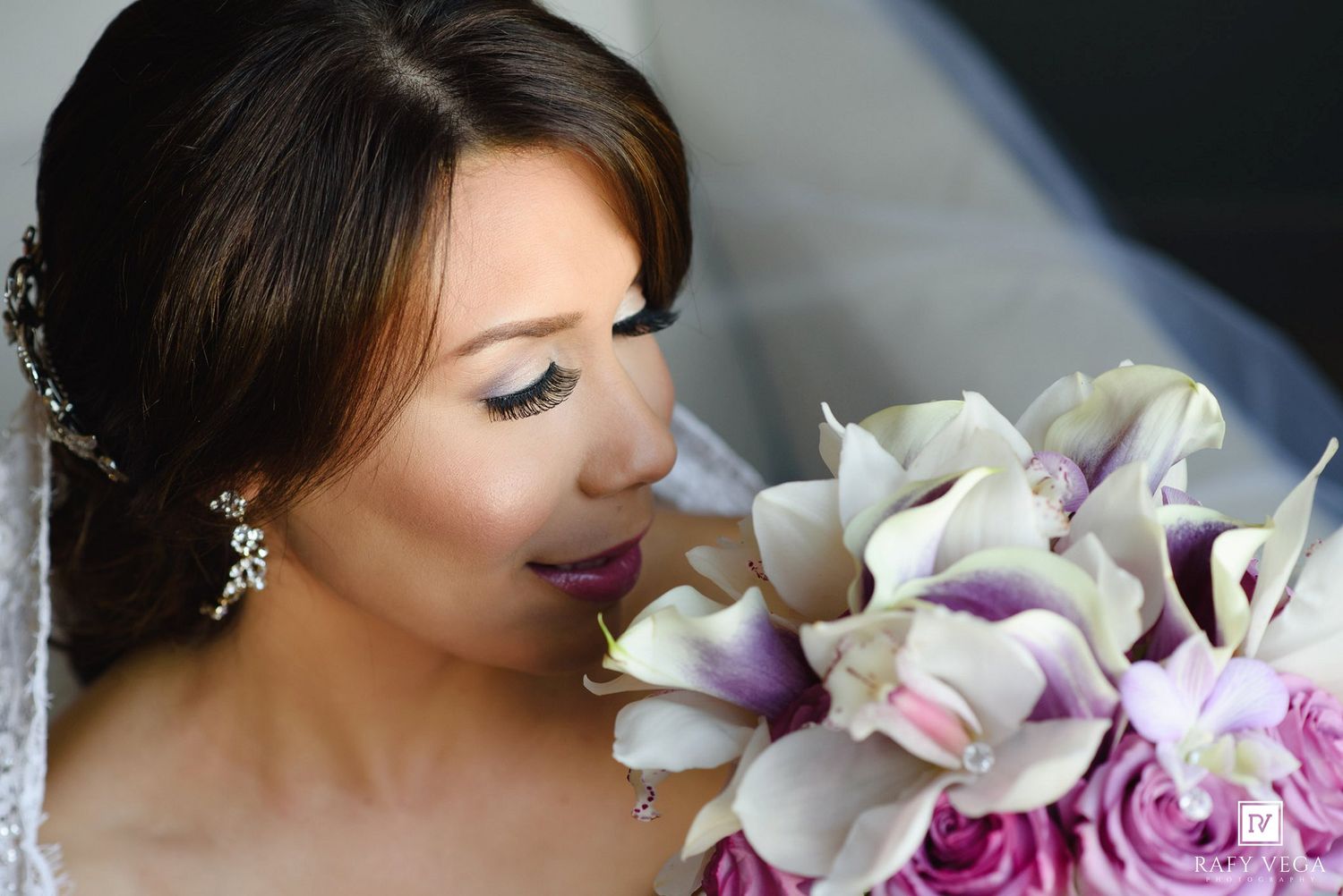Bride with elegant makeup holding a bouquet of purple and white orchids and roses on her wedding day.