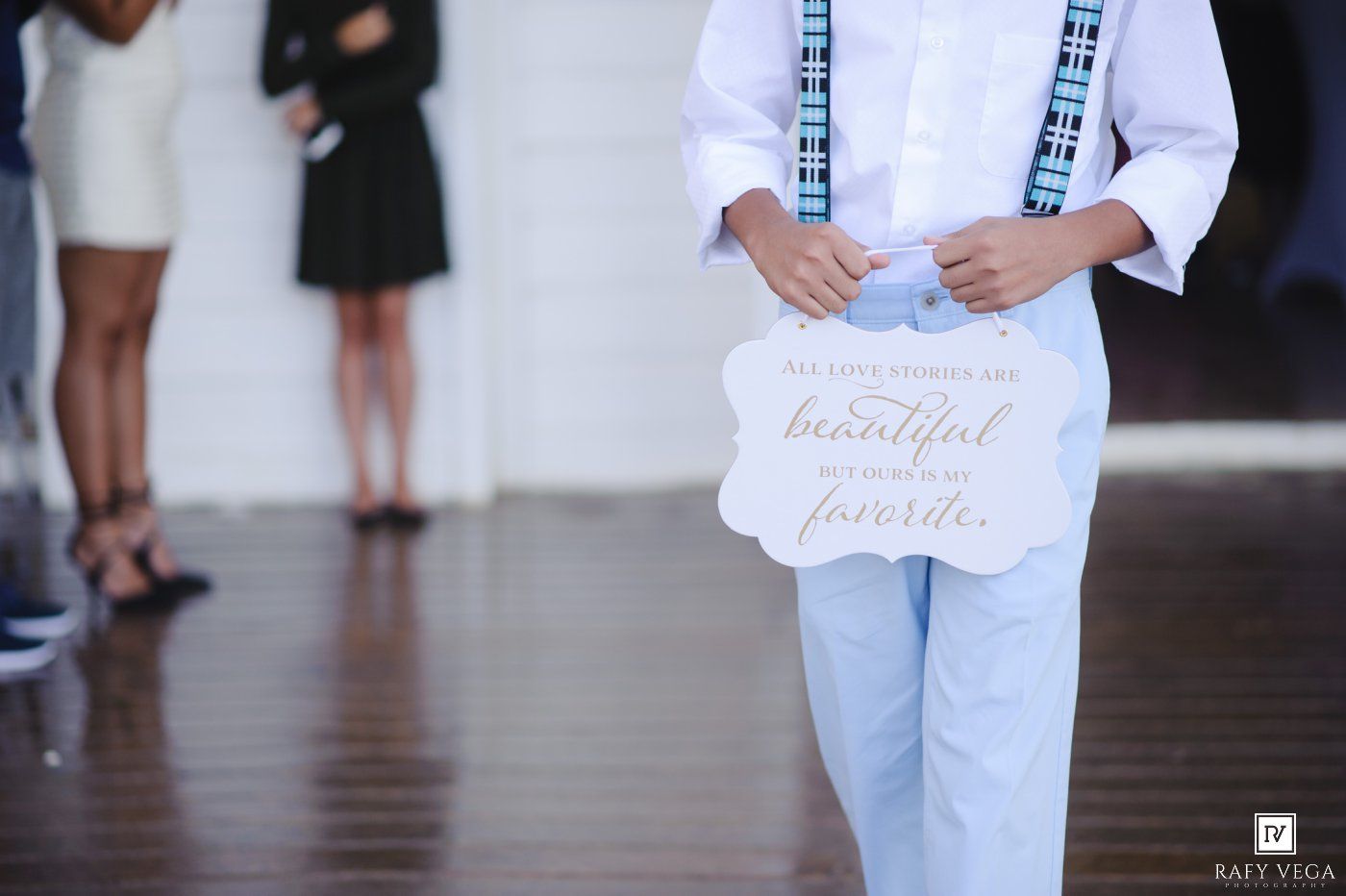 Young ring bearer in white shirt and blue pants holds decorative wedding sign at elegant venue.