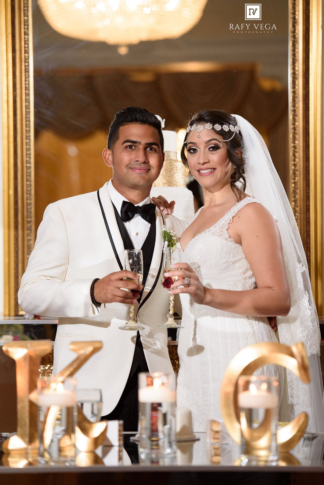 Bride and groom in elegant wedding attire toasting with champagne glasses at a luxurious gold-decorated reception venue.