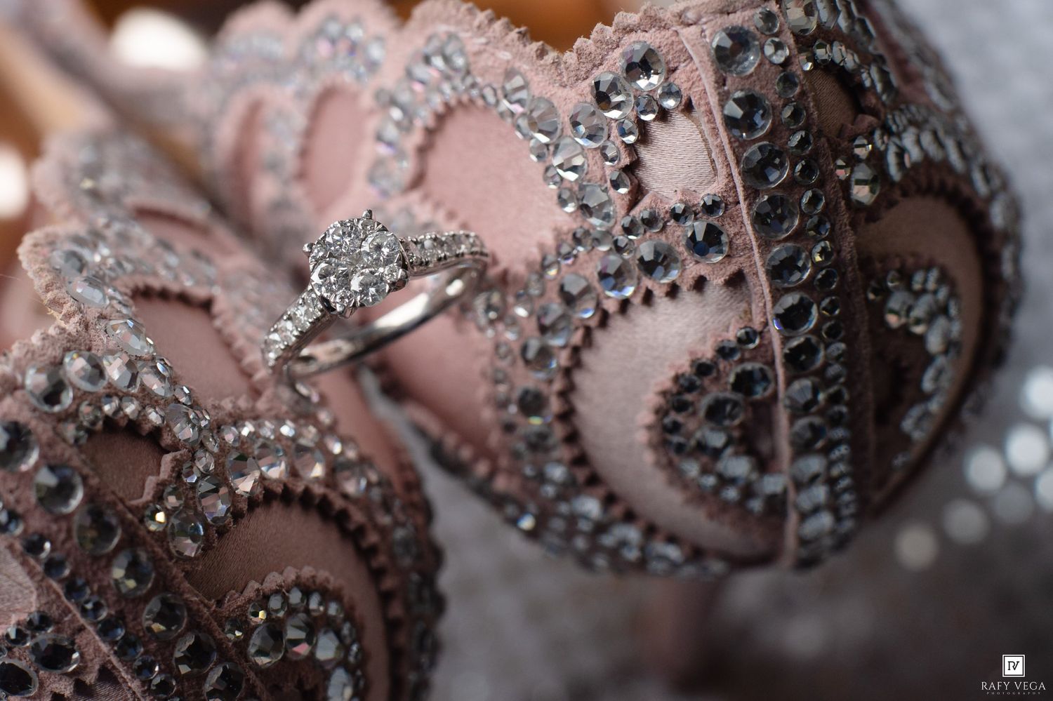 Diamond engagement ring resting on pink beaded wedding shoes adorned with silver rhinestone embroidery detailing.