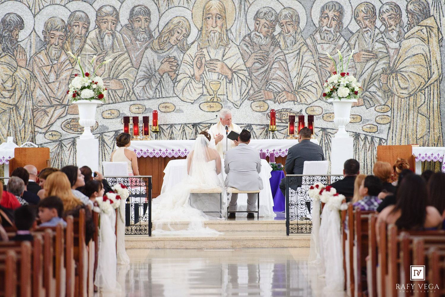 Bride and groom exchange vows at ornate church altar with mosaic backdrop during wedding ceremony.