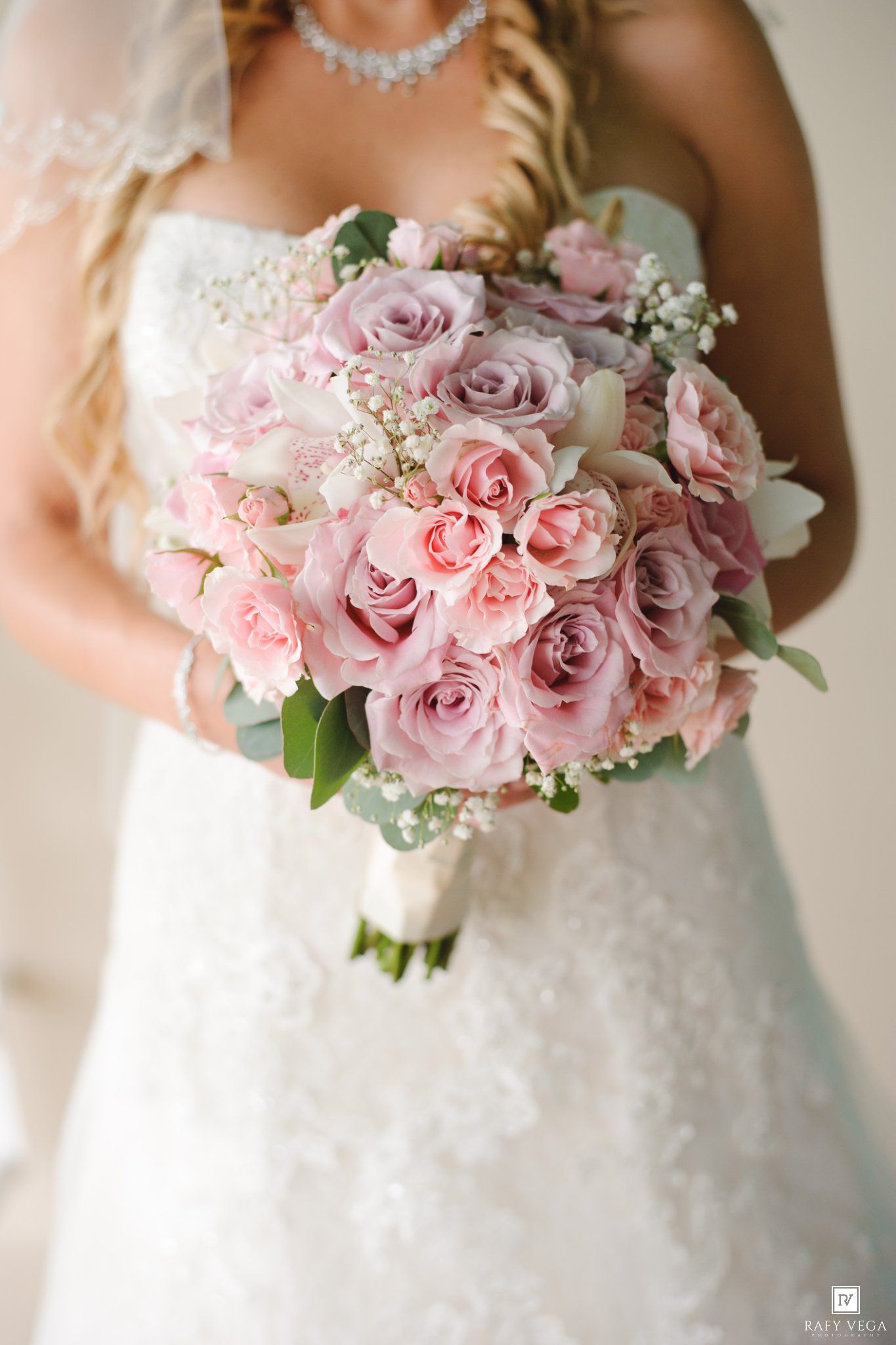 Bride holding a lush pink and lavender rose bouquet with baby's breath, wearing a lace wedding gown.