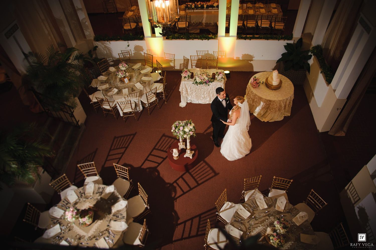 Aerial view of wedding reception hall with bride and groom sharing first dance among round guest tables.