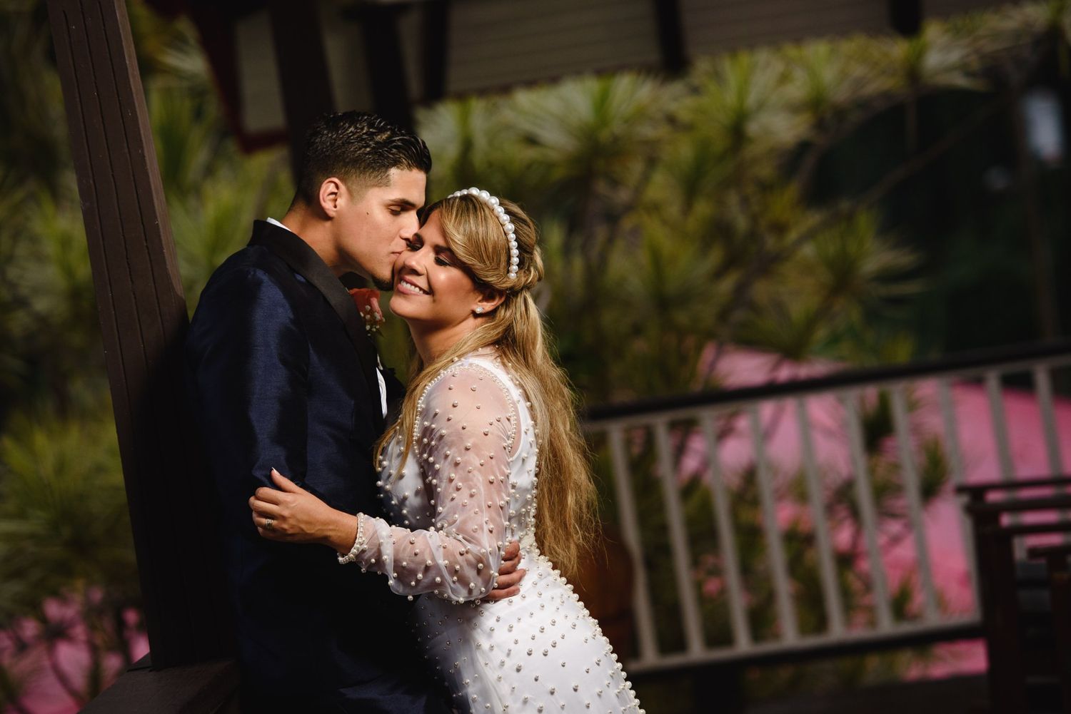 Bride and groom sharing a romantic kiss outdoors at night, bride wearing white lace gown with pearl headpiece.