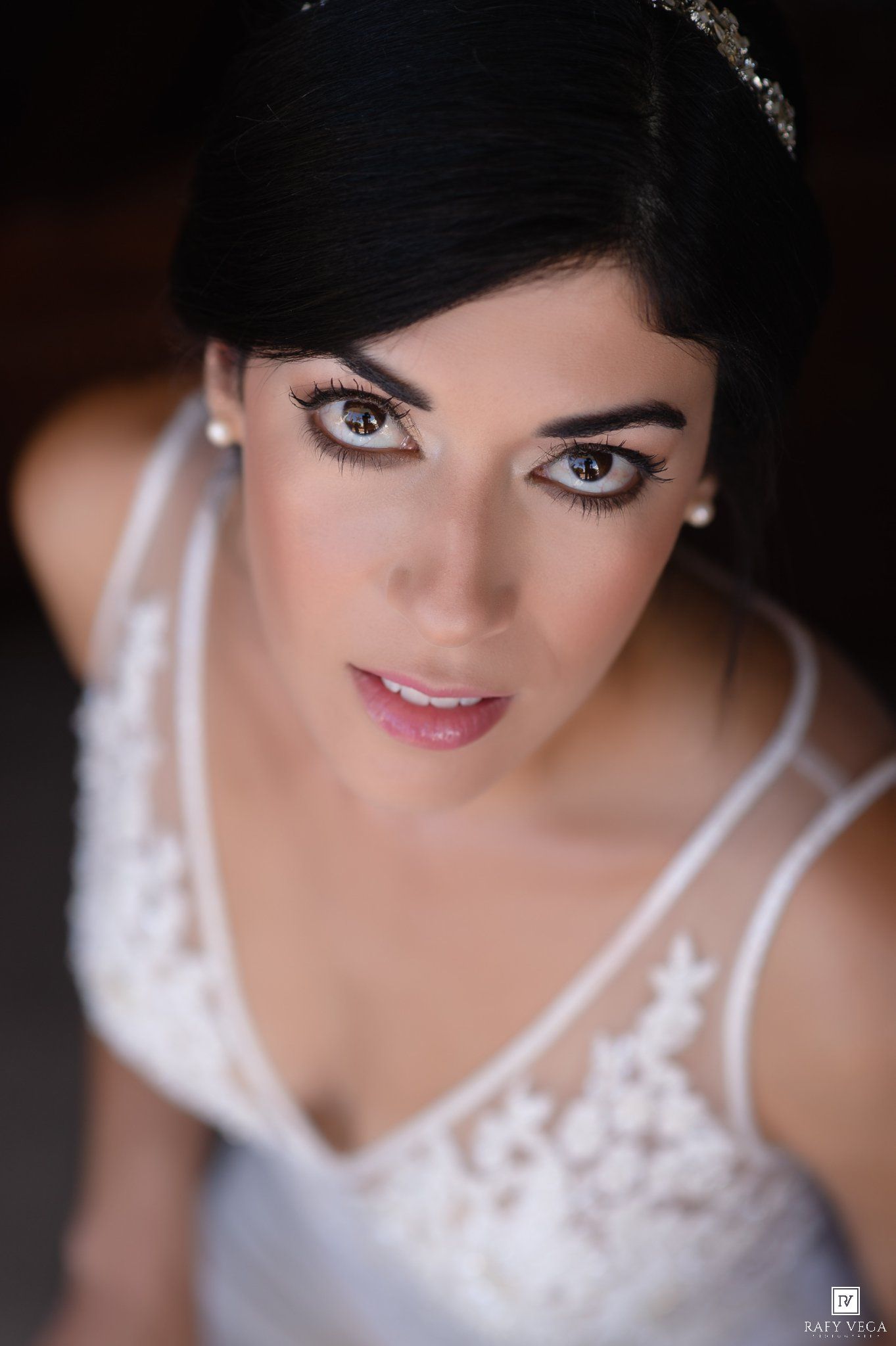 Close-up portrait of a beautiful bride in white lace dress with elegant makeup and dark hair adorned with a tiara.