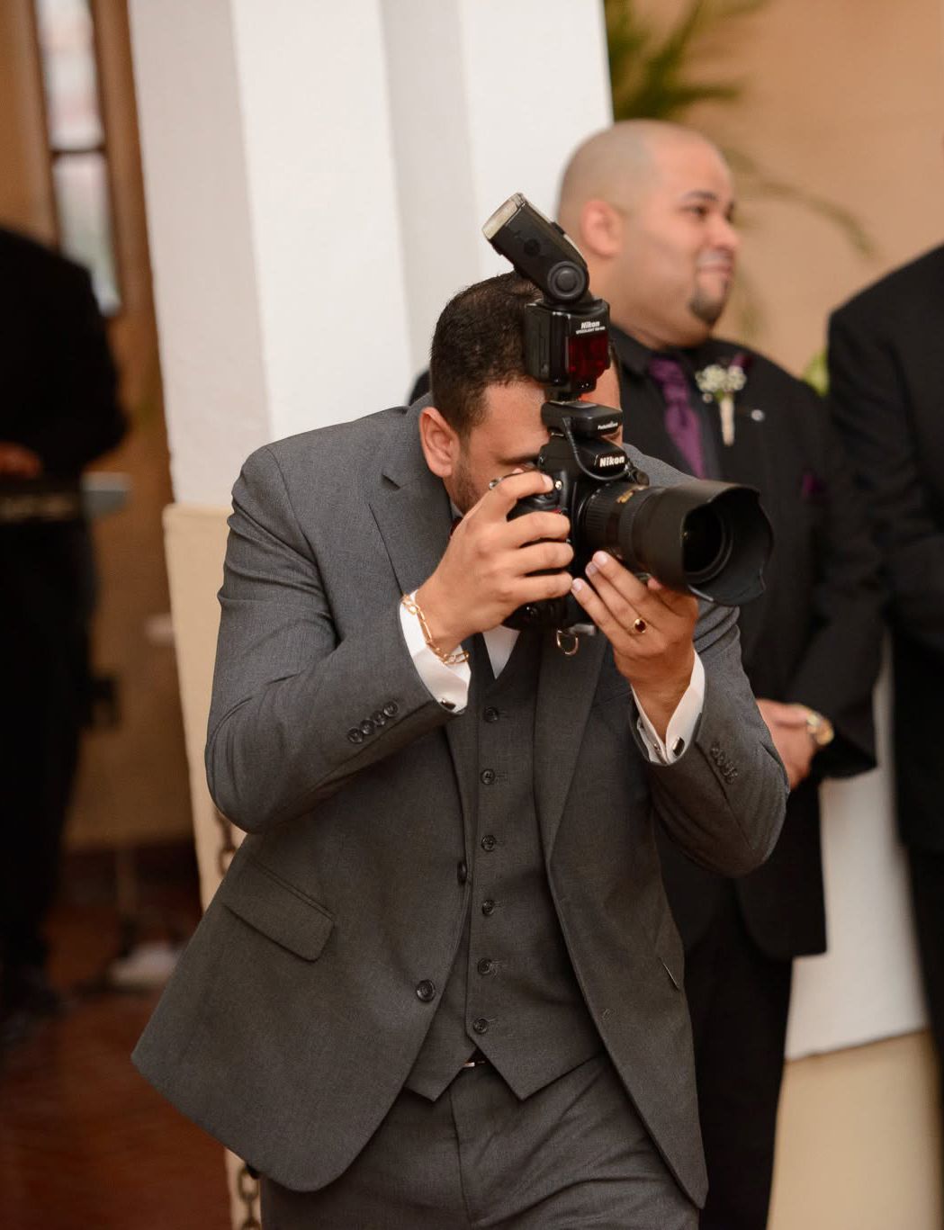 Man in gray suit photographing with professional DSLR camera and flash at a formal wedding event.
