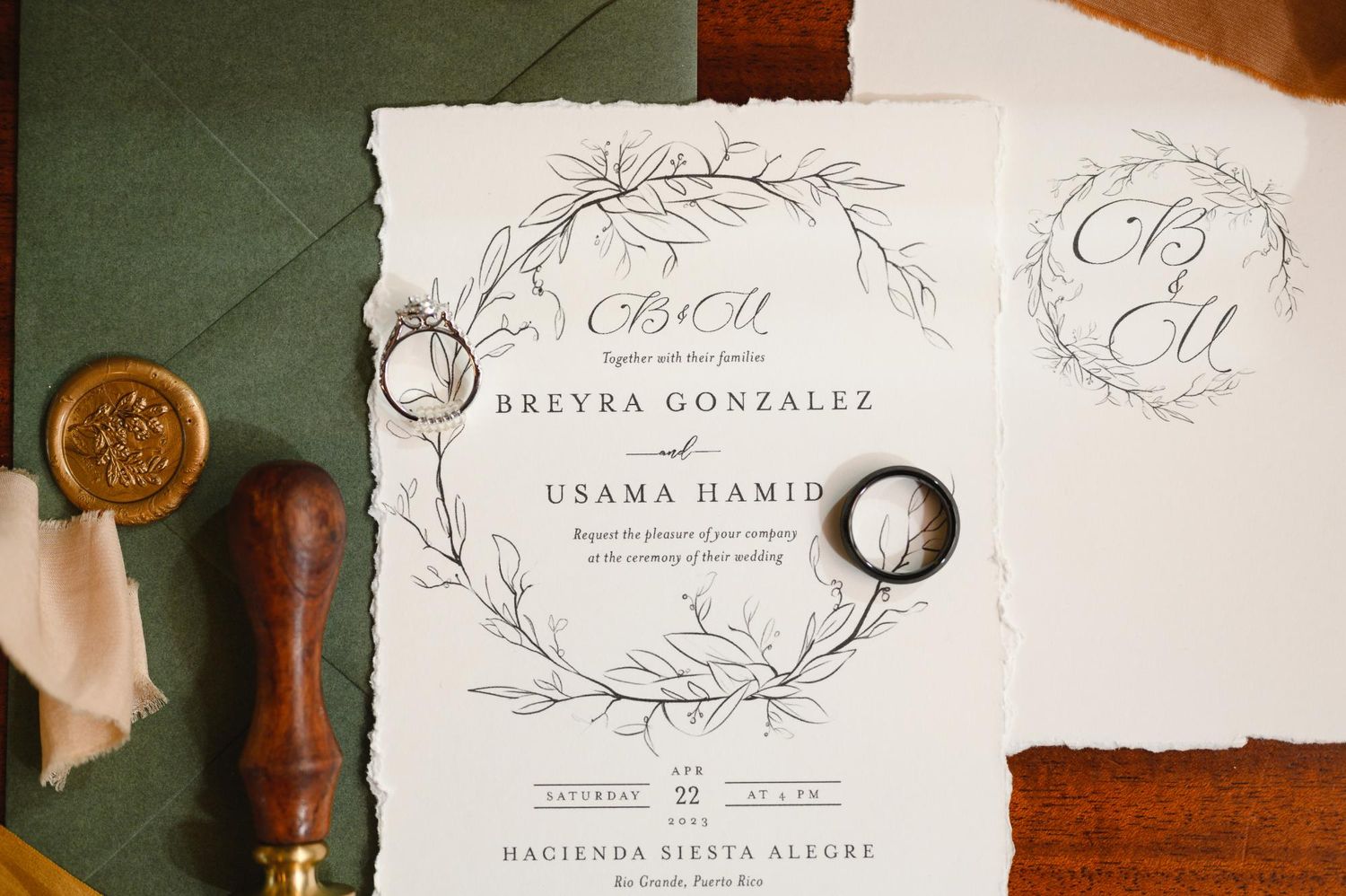 Elegant wedding invitation suite for Breyra Gonzalez and Usama Hamid with botanical wreath design, wax seal, and gold rings.