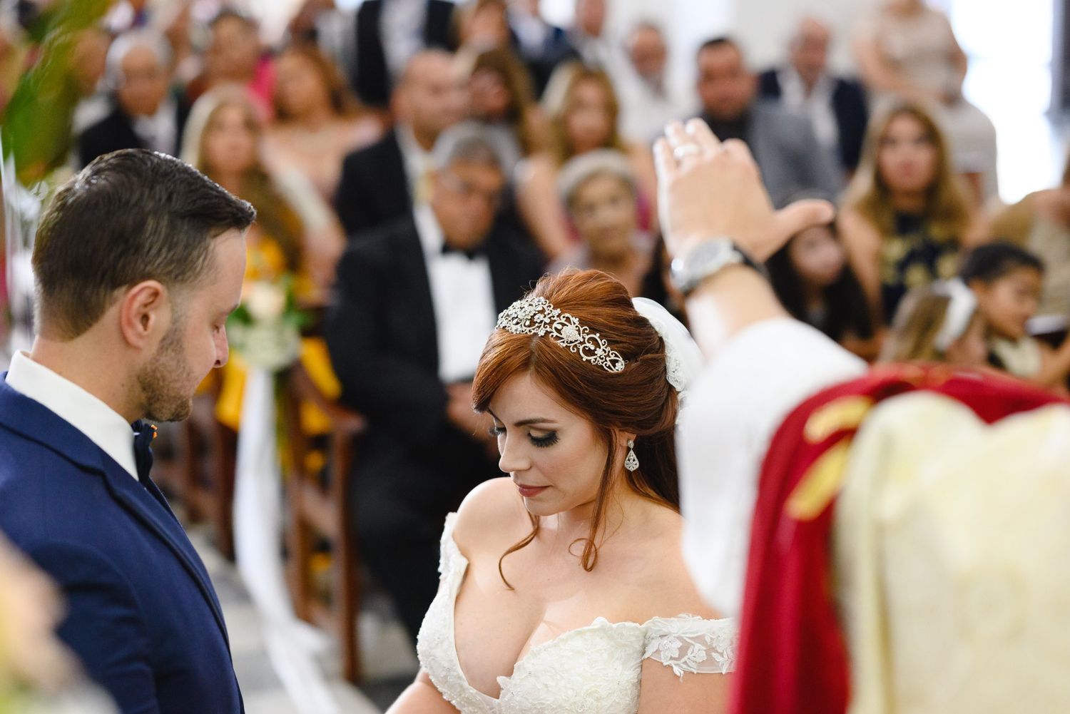Bride and groom at church wedding ceremony with officiant blessing the couple before guests.